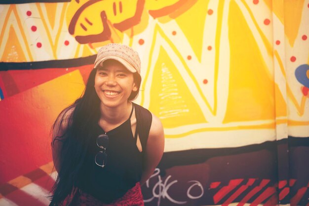 Photo portrait of smiling young woman standing against graffiti wall