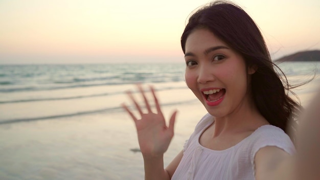 Portrait of smiling young woman standing at beach against sky during sunset