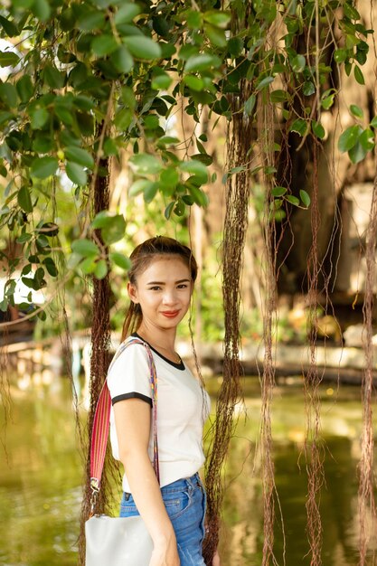 Portrait of smiling young woman standing by lake in park