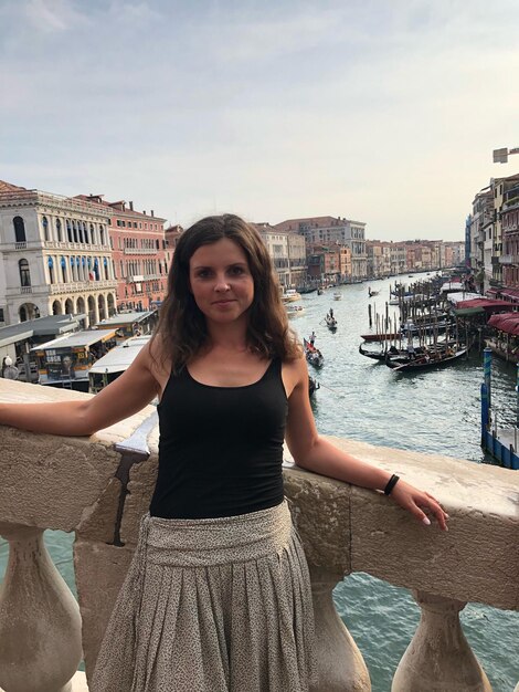 Portrait of smiling young woman standing in city against sky