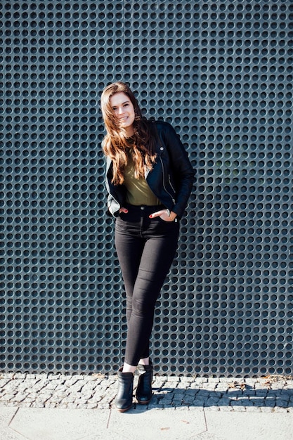 portrait of smiling young woman standing on footpath against wall