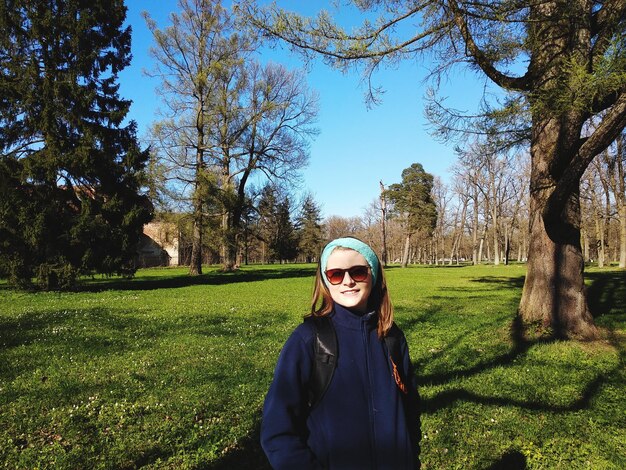 Photo portrait of smiling young woman standing on grassy field against trees