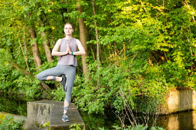 Portrait of smiling young woman standing on one leg against trees