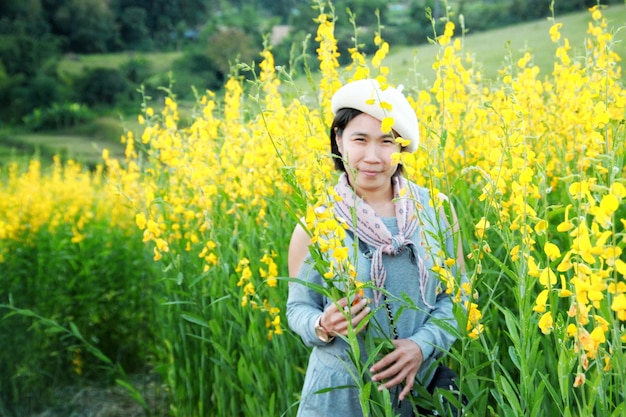 黄色い花の植物の中に立っている笑顔の若い女性の肖像画