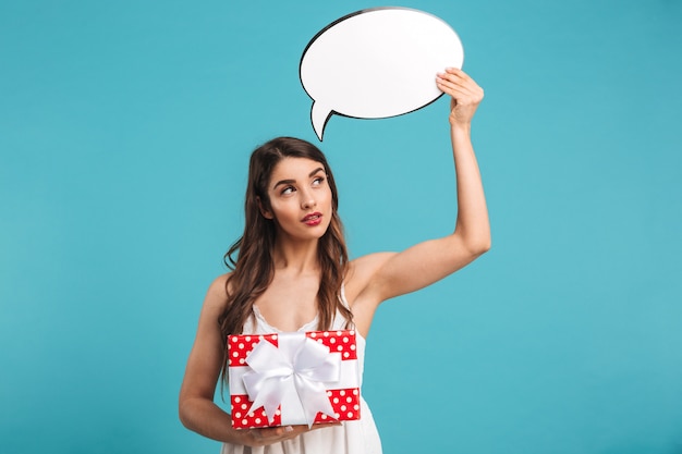 Portrait of a smiling young woman in summer dress holding a gift box and speech bubble