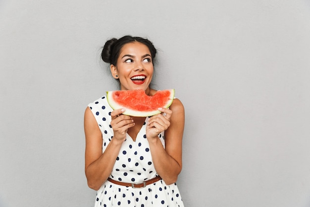 Photo portrait of a smiling young woman in summer dress isolated, holding watermelon slice