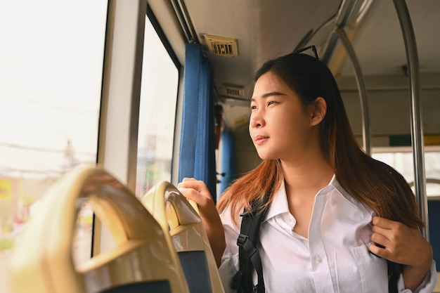 버스를 타고 통근하는 동안 창문으로 바라보는 미소 짓는 젊은 여성 관광객의 초상화
