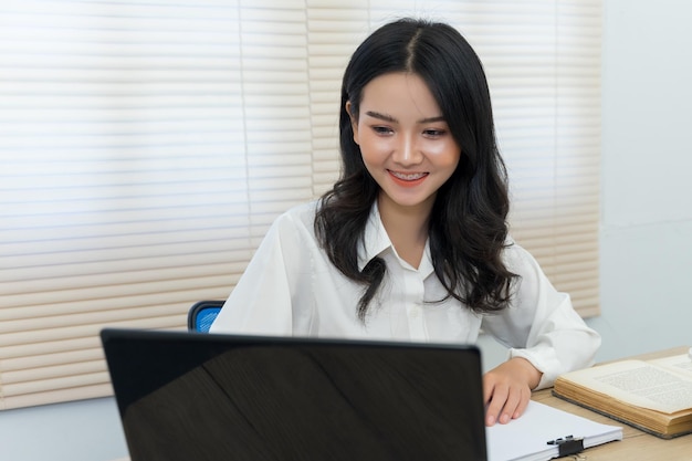テーブルの上にラップトップを使った笑顔の若い女性の肖像画