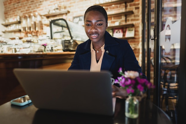 Портрет улыбающейся молодой женщины, использующей ноутбук и разговаривающей по мобильному телефону в кафе