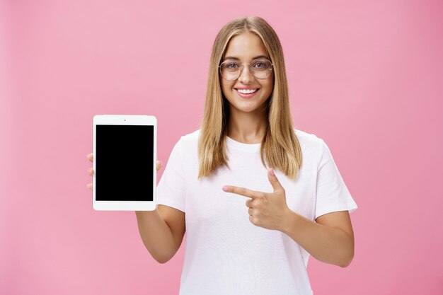 ピンクの背景にスマートフォンを使った笑顔の若い女性の肖像画