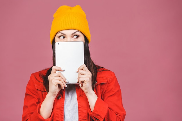 Portrait of a smiling young woman using tablet computer isolated on a pink wall.