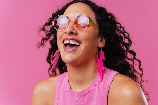 Photo portrait of smiling young woman wearing sunglasses against pink background