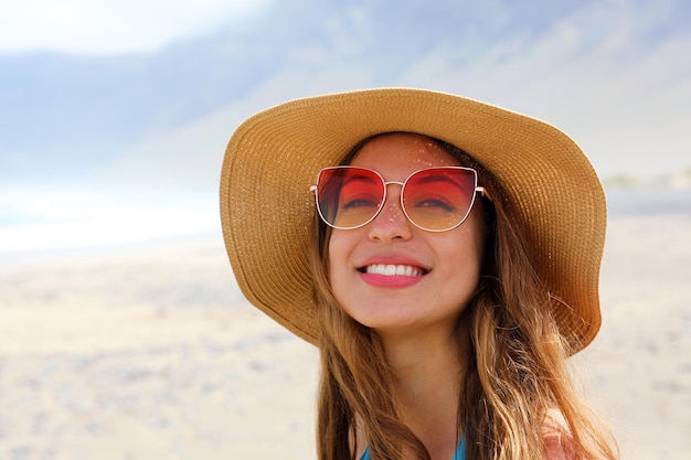 ビーチでサングラスと帽子をかぶった笑顔の若い女性の肖像画