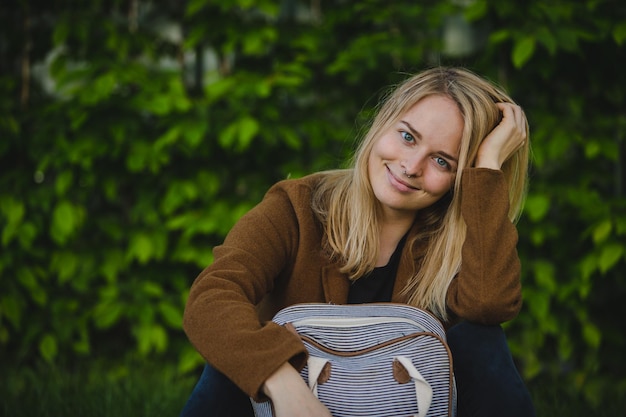 Portrait of smiling young woman with blond hair sitting against plants