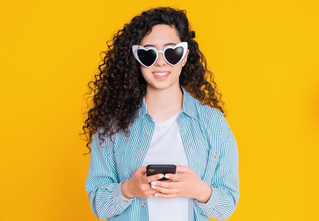Portrait of smiling young woman with curly hair using mobile phone against colored background