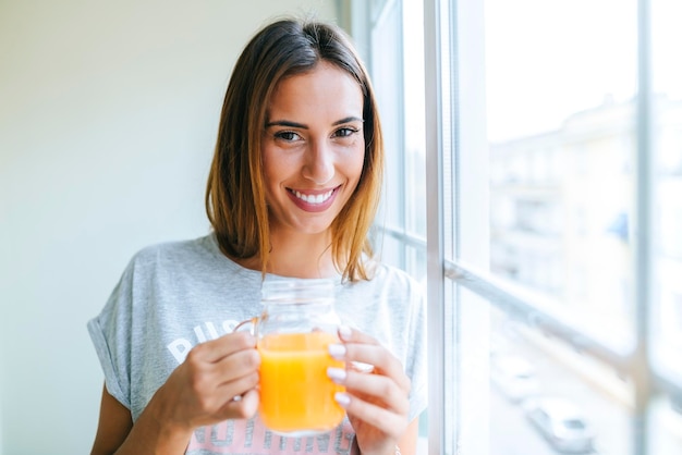 Photo portrait of smiling young woman with glass of orange juice