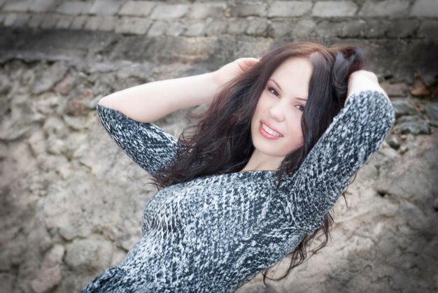 Photo portrait of smiling young woman with hands in hair against wall