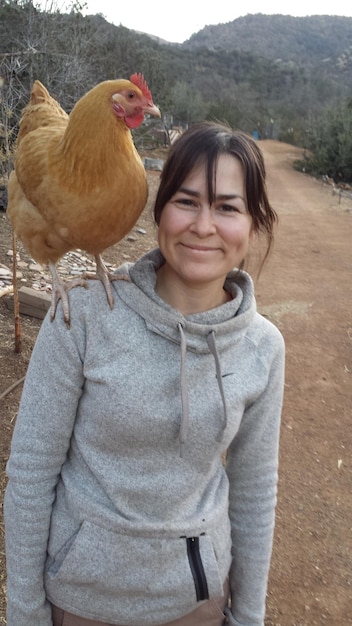 Photo portrait of smiling young woman with hen on shoulder
