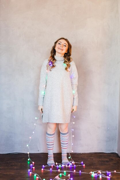 Photo portrait of smiling young woman with illuminated lights standing against wall