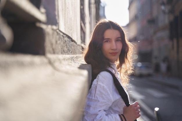 Portrait of Smiling Young woman with long Hair Wearing backpack and Leaning Against Wall