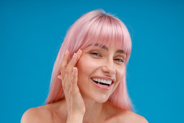 Portrait of smiling young woman with pink hair touching her perfect skin looking at camera posing