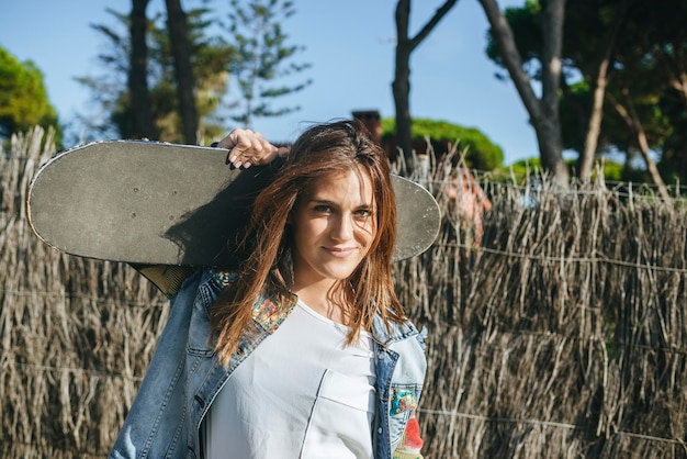 Portrait of smiling young woman with skateboard on her shoulders