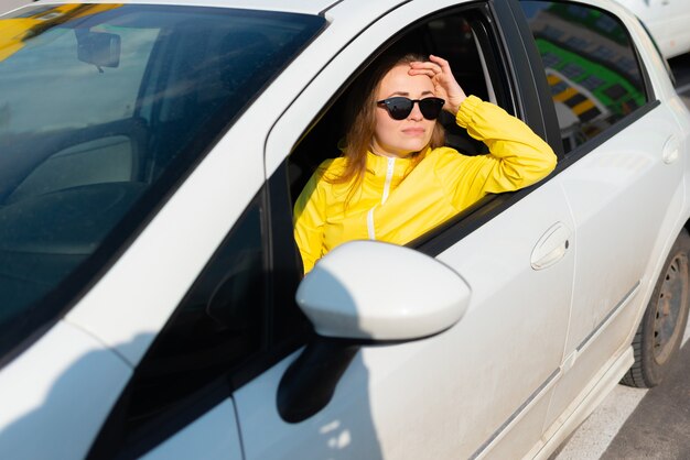 Portrait of smiling young woman in a yellow jacket wearing sunglasses sitting in her car