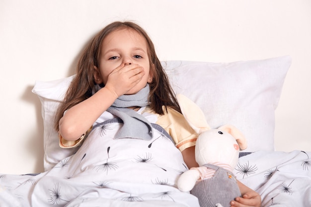 Photo portrait of sneezing child, covering her mouth with hand