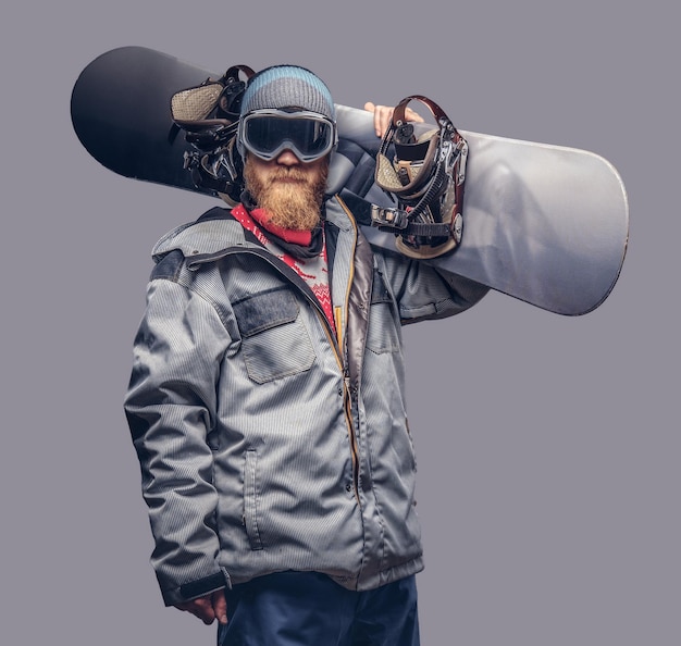 Portrait of a snowboarder dressed in a full protective gear for\
extream snowboarding posing with a snowboard on his shoulder at a\
studio. isolated on a gray background.