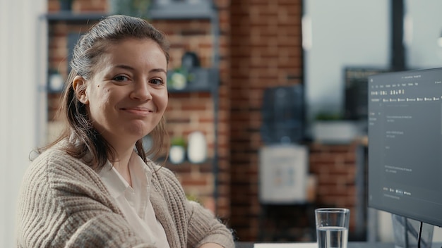 コンピューターのキーボードで頭を回してカメラに微笑んでプログラミング言語を入力するソフトウェア開発者の肖像画。デスクコンピューティングのビッグデータに自信を持って座っているカジュアルなデータベース管理者。