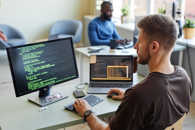 Photo portrait of software engineer writing code at workplace in office with multiple devices