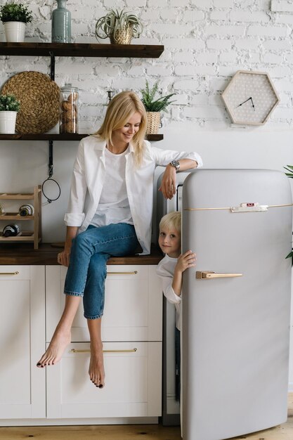 Foto ritratto del figlio nascosto nel frigorifero mentre la madre è seduta sul bancone della cucina a casa