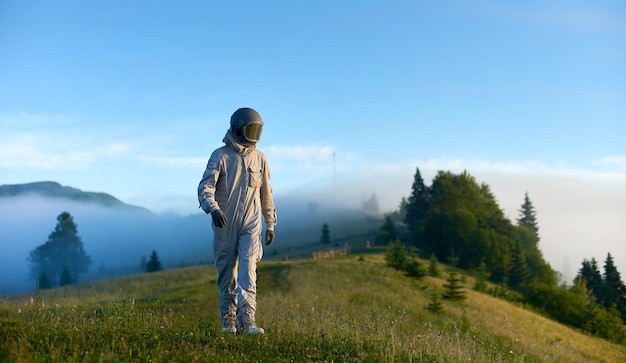 Ritratto di astronauta che indossa una tuta spaziale bianca e un casco che cammina da solo in una soleggiata radura di montagna verde