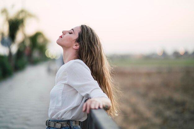 Portrait of a Spanish woman with long highlighted hair leaning on a pavement fence