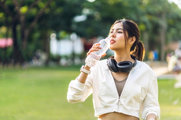 写真 肖像画スポーツアジアの美しさボディスリムな女性がリラックスして夏の緑の公園で緑の自然の背景に新鮮な気分でボトルから水を飲む健康的なライフスタイルのコンセプト