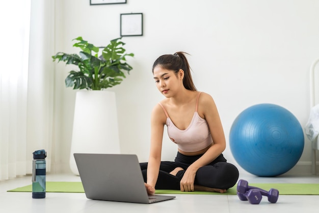 Portrait sport asian beauty body slim woman in sportswear sitting relax and girl practicing yoga and do fitness exercise with laptop computer in bedroom at homeDiet conceptFitness and healthy