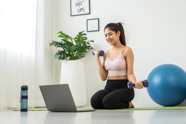 Portrait sport asian beauty body slim woman in sportswear\
sitting relax and girl practicing yoga and do fitness exercise with\
laptop computer in bedroom at homediet conceptfitness and\
healthy