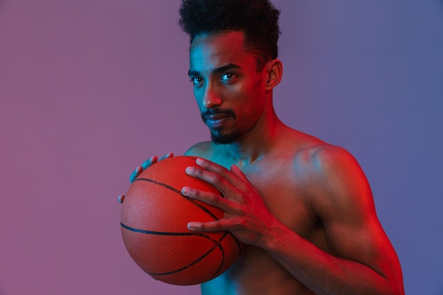 보라색 벽 위에 농구공을 들고 포즈를 취하는 스포츠 셔츠를 입지 않은 아프리카계 미국인 남자의 초상화
