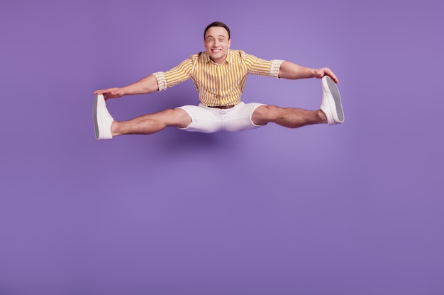 Photo portrait of sportive active flexible guy jump hands touch legs on purple background