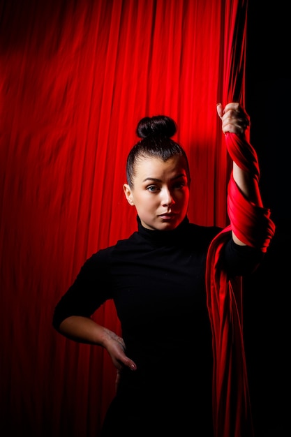 Portrait of a sports girl on a background of red cloths for aerial gymnastics. Studio shooting on a dark background,