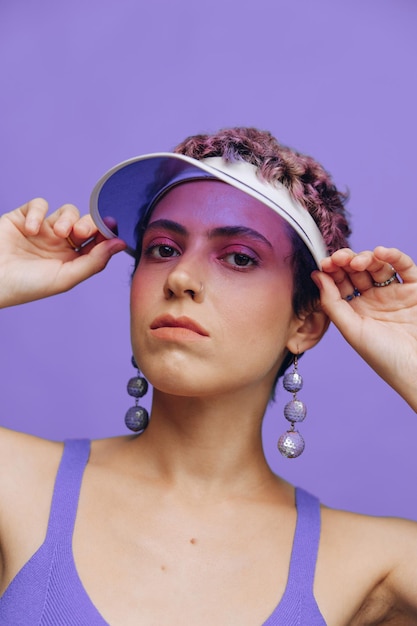 Портрет спортивной модницы, позирующей в фиолетовом спортивном костюме для йоги и прозрачной кепке на фиолетовом фоне. Монохромное фото высокого качества