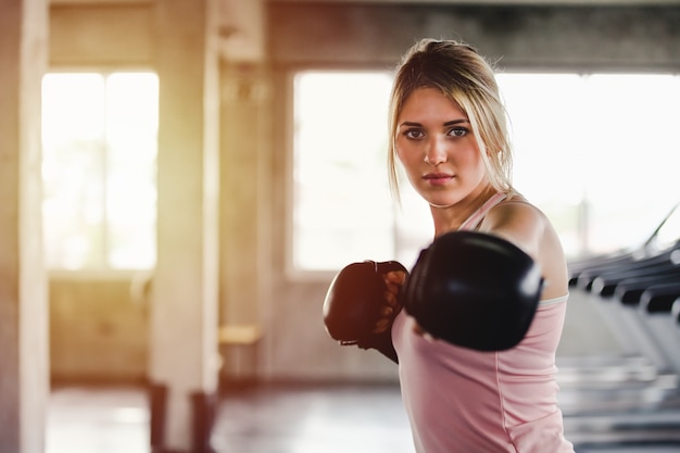 Ragazza sportiva del ritratto bella donna con i guantoni da pugile che si allenano in palestra