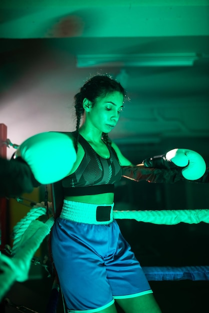 Portrait of sporty girl in corner of boxing ring. Young girl in sportswear standing holding ropes of ring, resting after tense bout, thoughtfully looking down. Extreme sport, healthy lifestyle concept