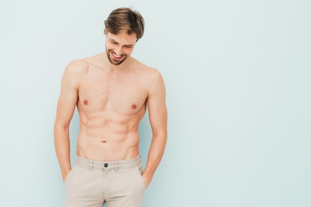 Portrait of sporty handsome strong man. Healthy smiling athletic fitness model posing near light blue wall