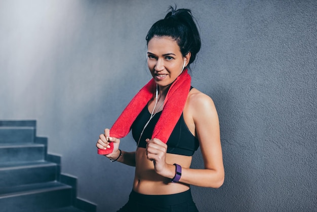 Portrait of sporty happy attractive brunette woman smiling with red towel on neck after workout in the gym Sport fitness lifestyle people concept