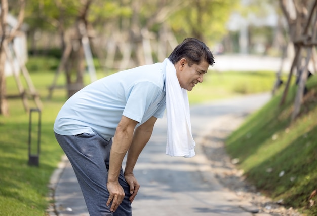 Portrait of sporty healthy mature male in hoodie and running shoes exercising outdoors, practicing side lunges. Elderly bearded man in sportswear warming up before morning run in park