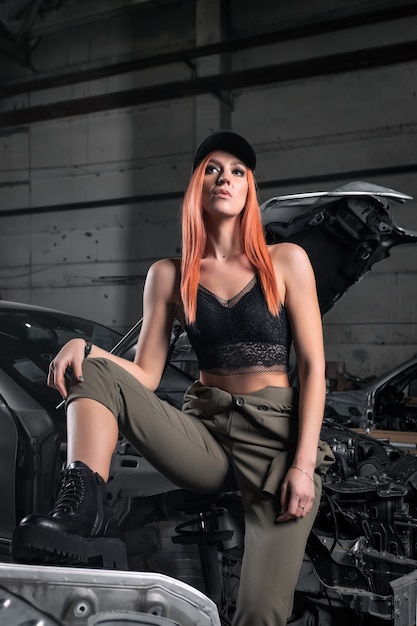 Portrait of a sporty woman in jeans and top stands with  disassembled car in the garage.