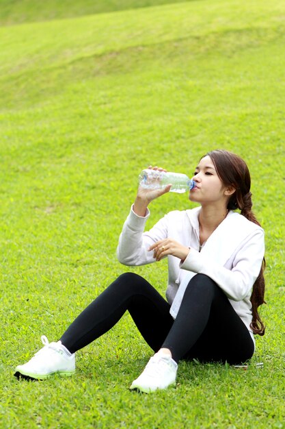 Portrait of sporty woman sitting on the grass and get refreshment after workout with copyspace