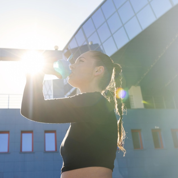 Photo portrait of a sporty woman who drinks water from a bottle outside the concept of metabolism after a long workout square photo