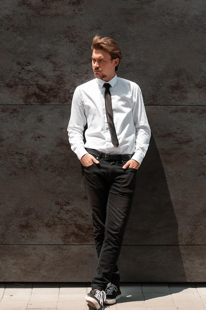 Портрет начинающего бизнесмена в белой рубашке с черным галстуком, стоящего перед серой стеной снаружи. Качественное фото